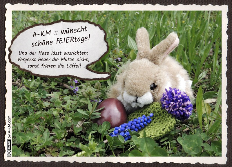 Plüschhase sitzt mit Osterei und Wollmütze im Gras - und schaut mürrisch.